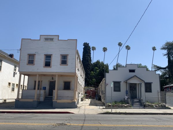 Two story and one story white boarding houses with stepped roofs.