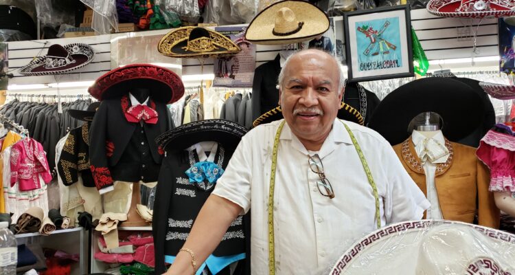 A smiling man with a mustache standing behind a counter of a store with mariachi hats.