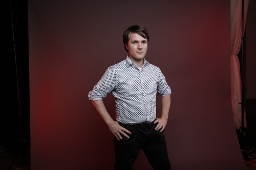 A young man with brown hair and light skin standing with hands on hips wearing a button-up shirt.