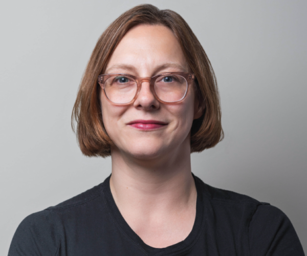 Portrait of a young woman with glasses and short red hair.