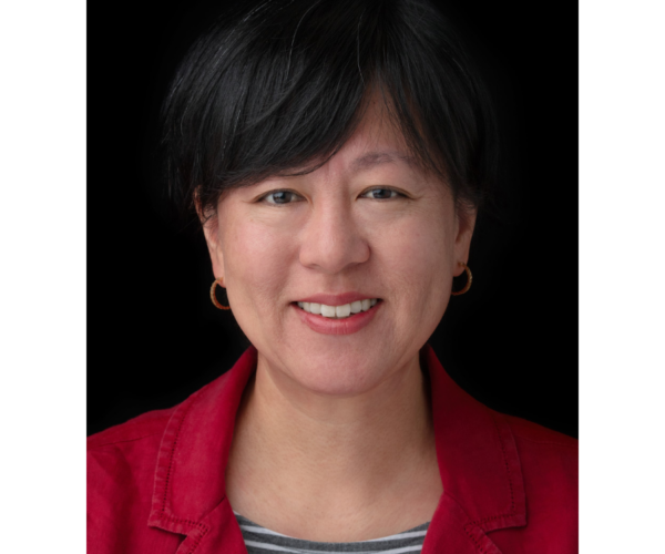 A woman smiling with a red jacket and a black and white striped shirt.