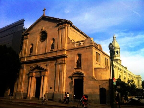 Two story stone church with pedestrians walking in front.