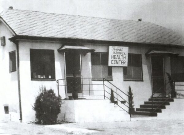 Black and white photo of a one-story building with two symmetrical staircases leading up to entrances. A sign reads, 