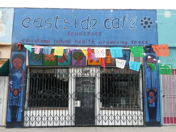 Blue-painted storefront that reads, Eastside Cafe. Papel picado hangs across entrance.