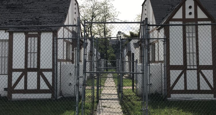 Derelict bungalow court behind chainlink fence