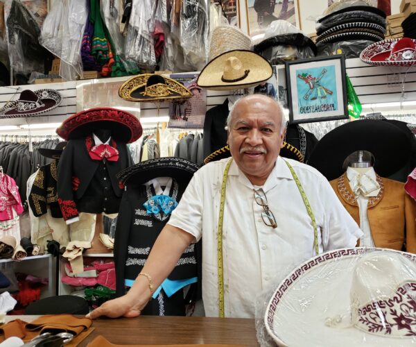 A smiling man with a mustache standing behind a counter of a store with mariachi hats.