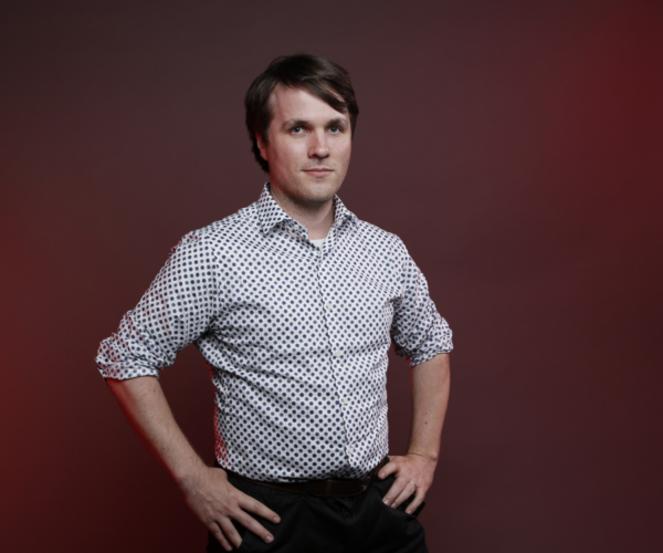 Portrait of a youg man in checkered shirt and black slacks.