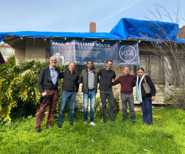 Image of six people standing in front of a modest home, banner behind reads 