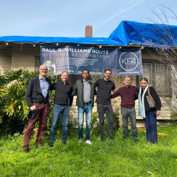 Image of six people standing in front of a modest home, banner behind reads 