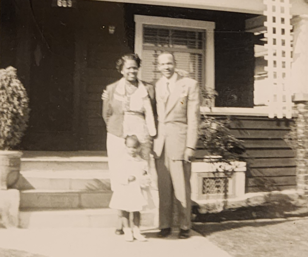 Black and white photo of an African American family outside of a craftsman style home.
