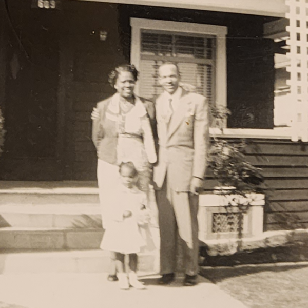 Black and white photo of an African American family outside of a craftsman style home.