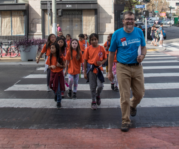 Students in orange shirts cross the street with an adult tour guide.