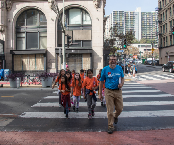 Students in matching shirts cross a downtown street with a Conservancy tour guide.