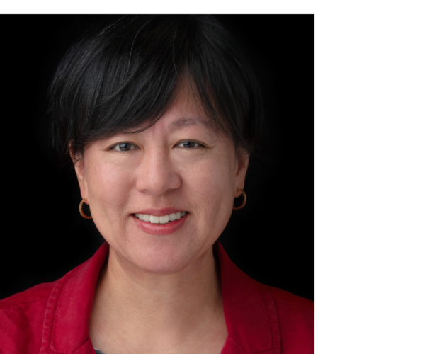 A woman smiling with a red jacket and a black and white striped shirt.