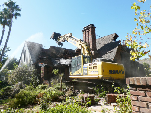 A yellow crane demolishing a house.