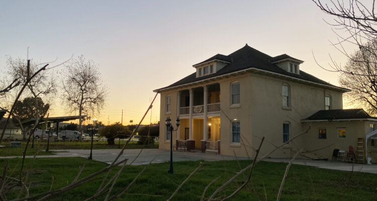 Two story Greek Revival house with sun setting behind it