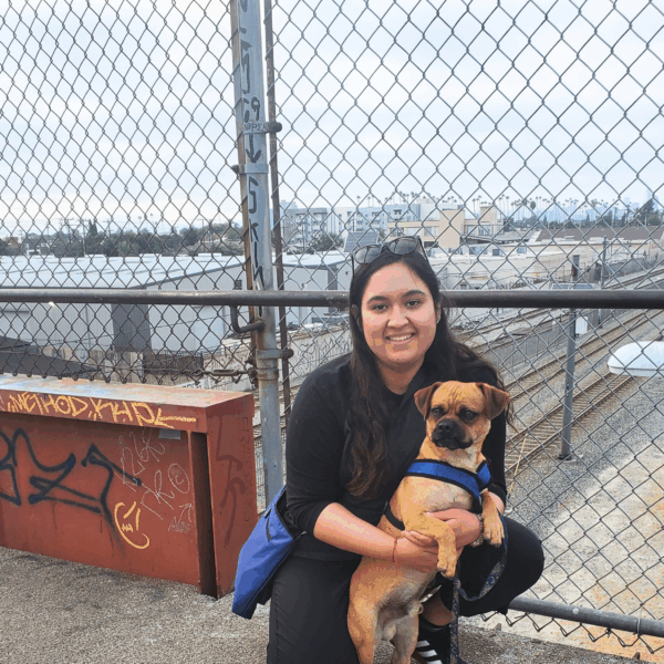 Woman holding a dog stands in front of a scenic city viewpoint.