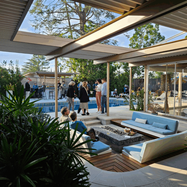 Several individuals standing together near a pool and fire pit, engaged in conversation during an outdoor event.