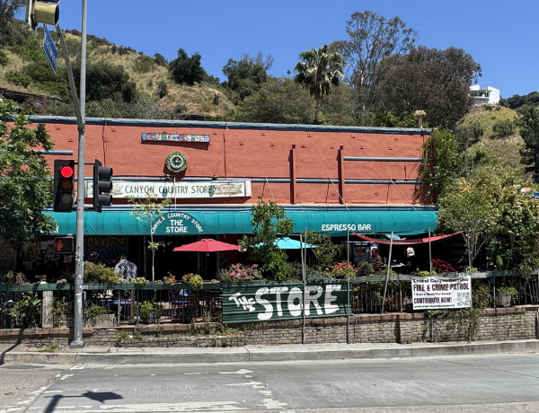 Masonry brick building with a smooth facade on the front primary elevation. The building includes a centered clock and canyon country store coca cola sign. There is a deck in front with ornamental plants surrounding the deck.